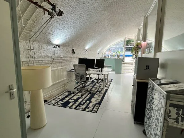 Modern ingerichte kantoorruimte in een gewelfde, witgemetselde ruimte onder een boog.